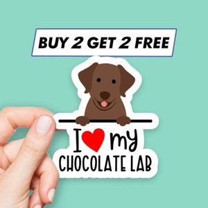 May include: A sticker featuring a cartoon chocolate Labrador with the text "I ❤️ my CHOCOLATE LAB". Above the sticker is a banner that reads "BUY 2 GET 2 FREE". The sticker is held by a hand against a teal background.