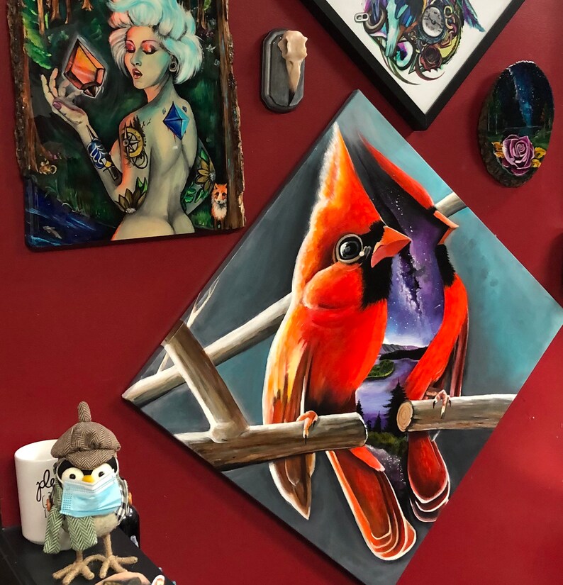 以下が含まれることがあります： 枝に止まっている2羽の赤い鳥の絵。左側の鳥は赤い体と黒い嘴、右側の鳥は紫色の体と黒い嘴をしている。背景は青と白の抽象的なデザインである。