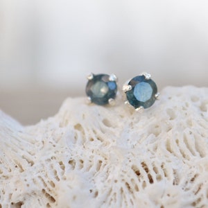 May include: A pair of silver stud earrings with a round, dark blue gemstone in each.