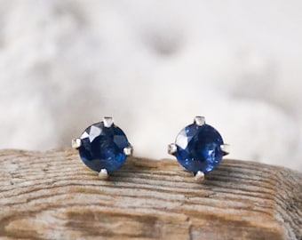 May include: A pair of silver stud earrings with round blue sapphire gemstones.