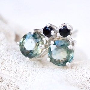May include: A pair of silver earrings with green and black gemstones. The earrings feature a cluster of three black gemstones and two larger green gemstones.