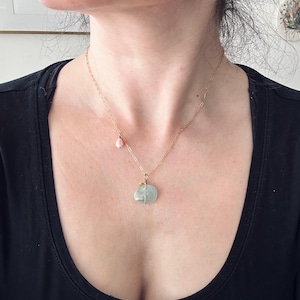 May include: A gold chain necklace with a light green stone pendant and a small pink stone charm.