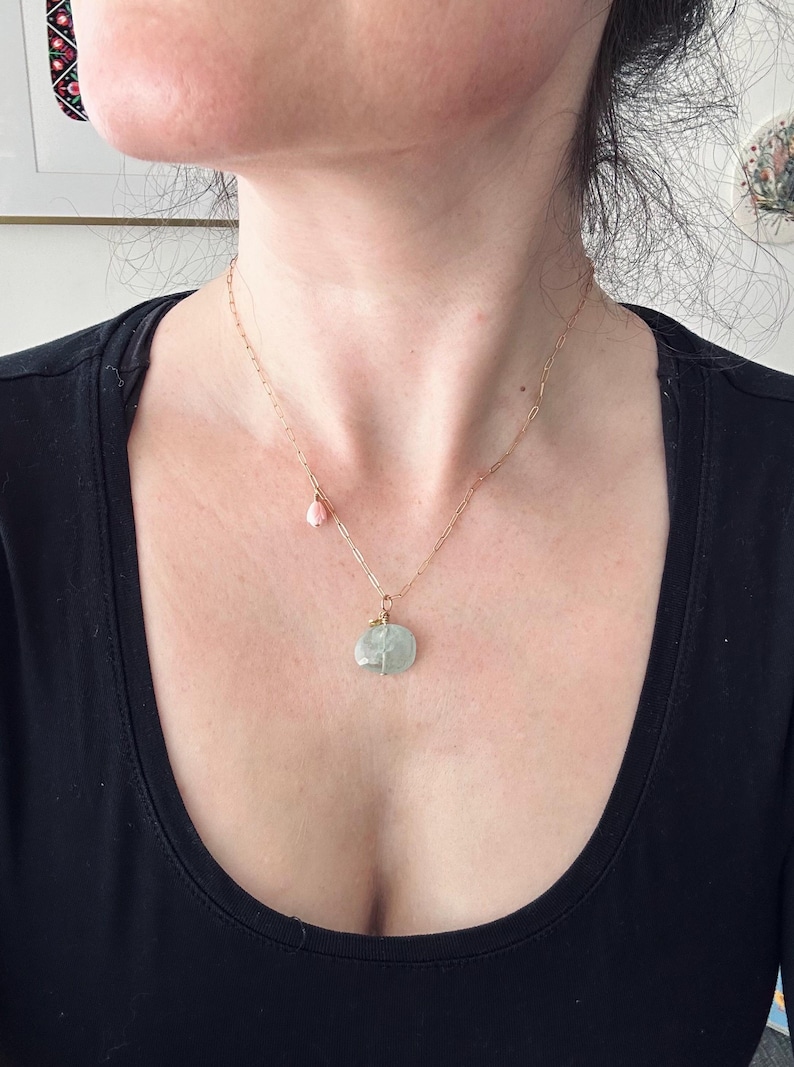 May include: A gold chain necklace with a light green stone pendant and a small pink stone charm.