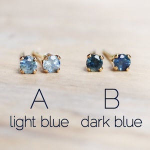 Puede incluir: Dos pares de pendientes de oro con piedras preciosas redondas azules. Los pendientes de la izquierda son de un tono azul m&aacute;s claro, etiquetados como "A azul claro". Los pendientes de la derecha son de un tono azul m&aacute;s oscuro, etiquetados como "B azul oscuro".