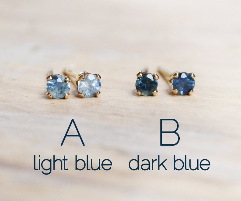 Puede incluir: Dos pares de pendientes de oro con piedras preciosas redondas azules. Los pendientes de la izquierda son de un tono azul m&aacute;s claro, etiquetados como "A azul claro". Los pendientes de la derecha son de un tono azul m&aacute;s oscuro, etiquetados como "B azul oscuro".