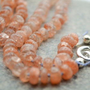 May include: A necklace made of orange sunstone beads with a silver clasp.