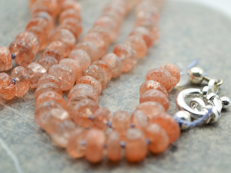 May include: A necklace made of orange sunstone beads with a silver clasp.