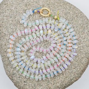 May include: A rainbow moonstone bead necklace with a gold clasp. The beads are strung on a thin, colourful thread.