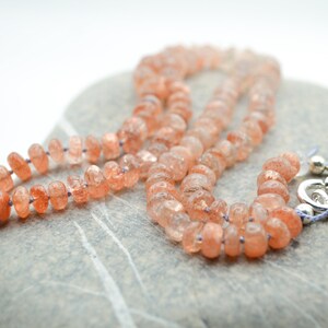 May include: A necklace made of orange sunstone beads with a silver clasp.