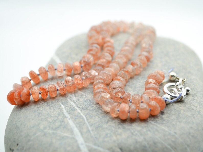 May include: A necklace made of orange sunstone beads with a silver clasp.