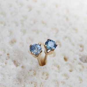 Puede incluir: Un par de pendientes de bot&oacute;n de oro con peque&ntilde;as piedras azules redondas.