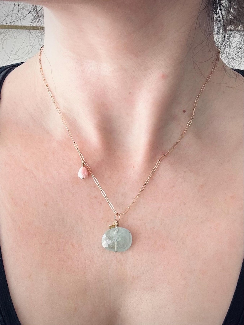 May include: A gold chain necklace with a light blue gemstone pendant and a small pink flower charm.