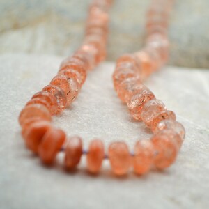 May include: A strand of orange sunstone beads, strung on a clear thread. The beads are faceted and have a translucent appearance.