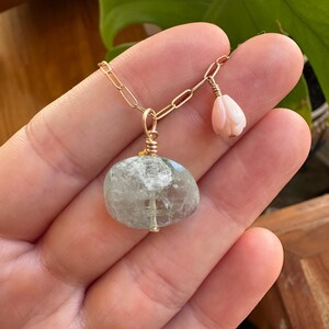 May include: A gold chain necklace with a light green gemstone pendant and a small pink shell charm.