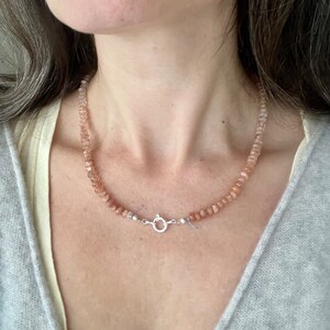 May include: A delicate necklace made of small, light pink and peach sunstone beads. The necklace has a silver clasp.