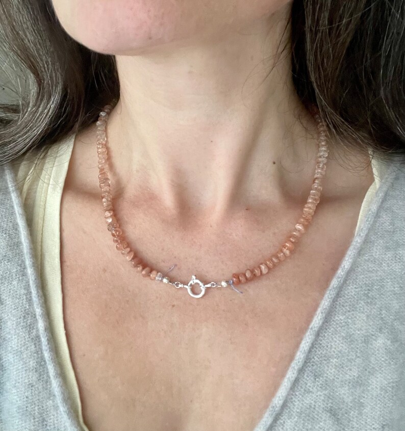 May include: A delicate necklace made of small, light pink and peach sunstone beads. The necklace has a silver clasp.