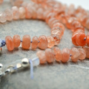 May include: A necklace made with orange sunstone beads and silver clasps. The beads are faceted and have a natural, rough texture.
