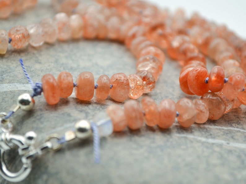 May include: A necklace made with orange sunstone beads and silver clasps. The beads are faceted and have a natural, rough texture.