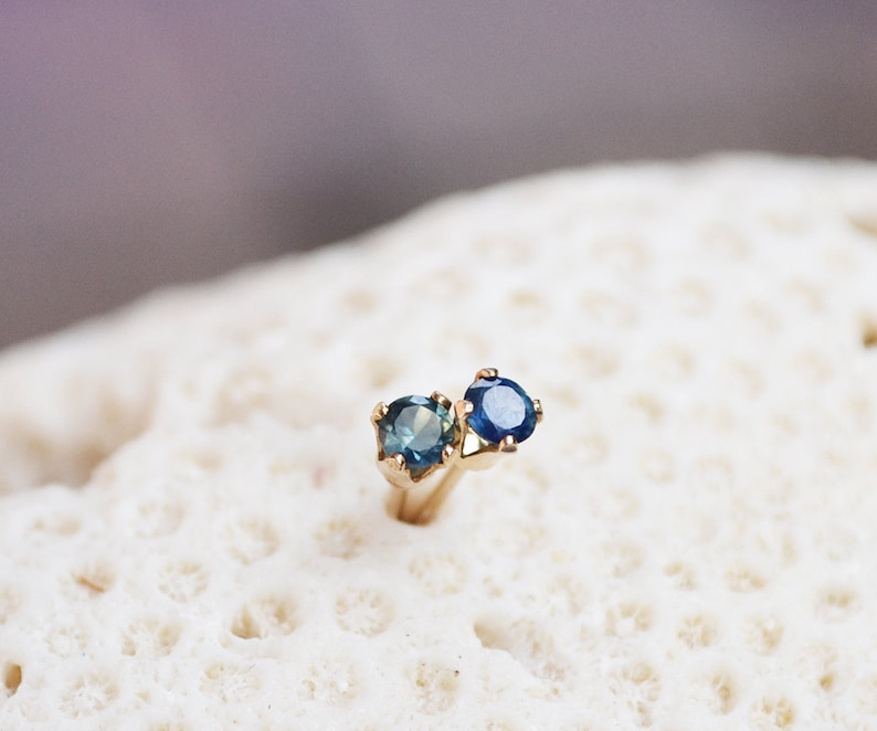 Puede incluir: Un par de pendientes de oro con piedras preciosas azules. Los pendientes est&aacute;n engastados con dos piedras redondas, una ligeramente m&aacute;s grande que la otra.
