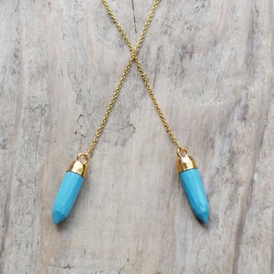 May include: A gold chain necklace with two blue crystal pendants. The crystals are faceted and have a gold-toned cap at the top.