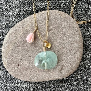 May include: A gold chain necklace with a light blue aquamarine pendant and a pink coral flower charm.