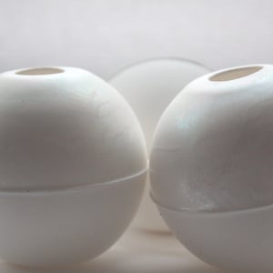Puede incluir: Dos bolas decorativas redondas, lisas y blancas con un acabado perlado.