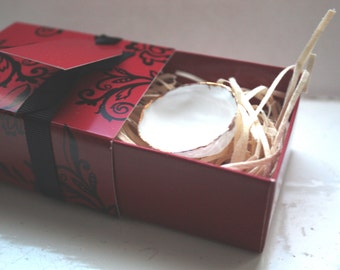 May include: A small white ceramic bowl with a gold rim sits inside a red box with black floral designs. The box is filled with shredded paper.