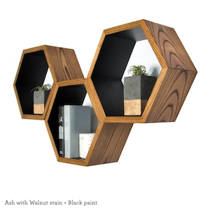 May include: A set of three hexagonal wooden shelves in a dark wood stain with black paint. The shelves are arranged in a staggered pattern and are decorated with potted plants and books.