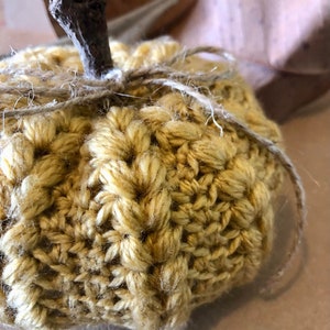 May include: A crocheted pumpkin in a yellow color with a brown twig stem and twine tied around the top.
