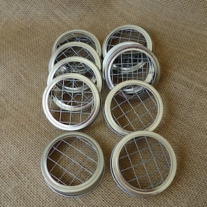May include: A set of 10 silver metal jar lids with a wire mesh insert. The lids are round and have a smooth, shiny finish.