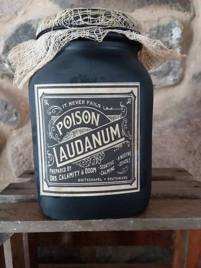 May include: A black glass jar with a white label that reads "IT NEVER FAILS POISON LAUDANUM PREPARED BY DRS. CALAMITY & DOOM SEDATIVE ANODYNE CALMING DEADLY WHITECHAPEL SOUTHWARK". The jar is wrapped in a beige burlap cloth.