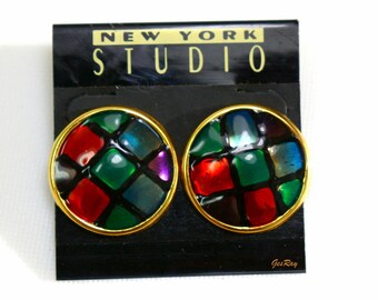 May include: A pair of round, gold-toned earrings with a stained glass design. The earrings feature a mosaic of red, green, blue, and black squares.