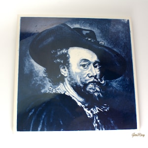 May include: Square ceramic tile featuring a portrait of a man in a wide-brimmed hat, rendered in shades of blue. The artwork depicts a man with a mustache and beard, wearing a dark coat and a ruffled collar. The tile has a white border.