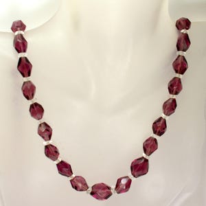 May include: A vintage necklace with faceted, deep purple beads. Small, silver-toned spacers separate the beads. The necklace is displayed on a white mannequin, highlighting its design and colour.