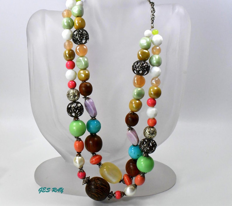 May include: A multi-strand necklace with colorful beads, including turquoise, green, pink, orange, and brown. The necklace features metal accents and a variety of bead shapes and sizes.