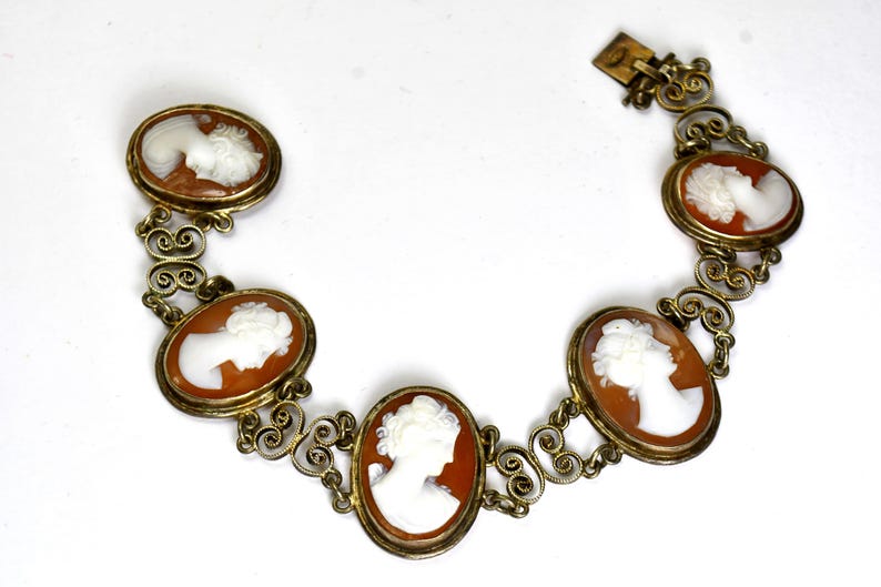 Peut inclure: Un bracelet vintage &agrave; cam&eacute;es avec six cam&eacute;es ovales, chacun pr&eacute;sentant un profil blanc dans des cadres dor&eacute;s. Le bracelet est reli&eacute; par des maillons en filigrane et poss&egrave;de un fermoir. Un bijou classique.