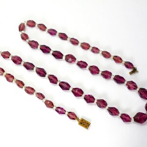 May include: A vintage necklace with faceted, deep purple beads and smaller white beads. The necklace has a gold-toned clasp. The beads are elongated and geometric. The necklace is displayed against a white background.