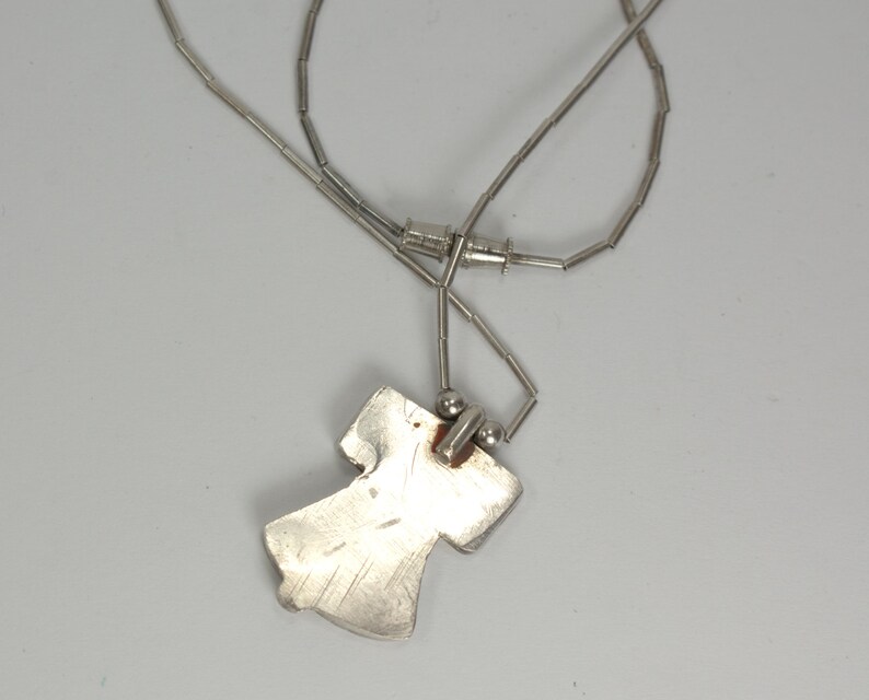 Peut inclure: Un collier en argent avec un pendentif en argent en forme de personne. Le pendentif est attach&eacute; &agrave; la cha&icirc;ne par un petit anneau en argent.
