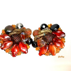 May include: A pair of round cluster earrings featuring a dense arrangement of multi-colored beads, including smooth red teardrop shapes, faceted black stones, clear crystals, and small orange glass beads, all accented with coiled gold-tone wire.