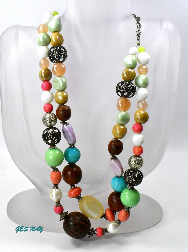 May include: A multi-strand necklace with a variety of colorful beads, including green, turquoise, pink, white, and brown. The necklace also features metal accents.