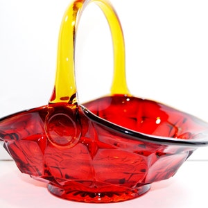 May include: A red glass basket with a yellow glass handle. The basket has a faceted design and a rounded base.