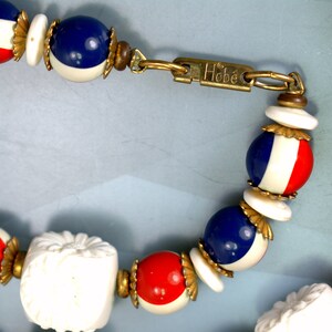May include: A vintage Hobe necklace with red, white, and blue beads. The beads are round and have a gold trim. The necklace has a clasp with the Hobe logo.