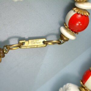 May include: A close-up of a red, white, and blue beaded necklace with a gold clasp. The clasp has the text "PATENT 3327601" engraved on it.