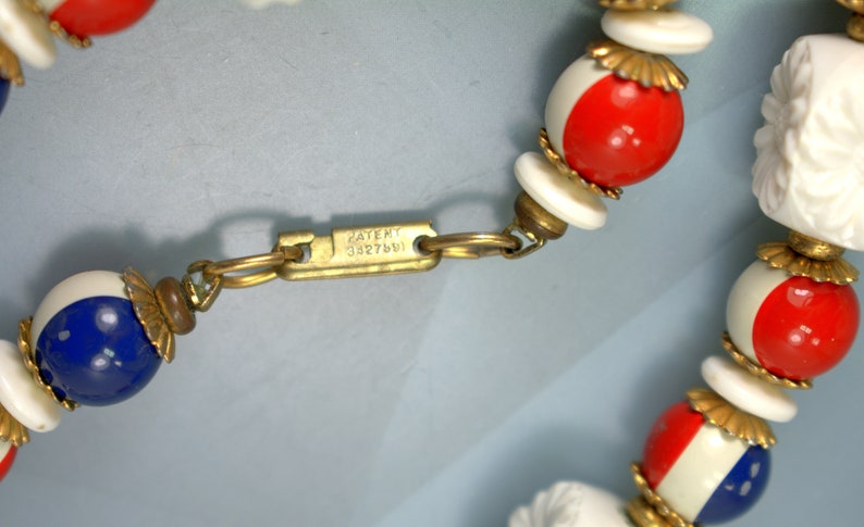 May include: A close-up of a red, white, and blue beaded necklace with a gold clasp. The clasp has the text "PATENT 3327601" engraved on it.