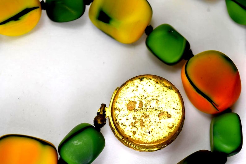 Op de afbeelding: Close-up van een vintage ketting met grote, kleurrijke kralen in geel, groen en oranje. De kralen zijn geregen met een goudkleurige sluiting. De ketting is waarschijnlijk een statement-sieraad.