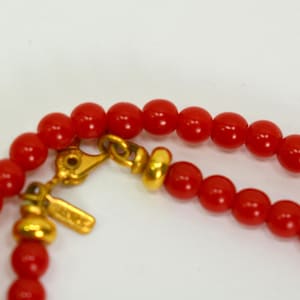 May include: A red beaded necklace with a gold clasp and a gold bead. The necklace is made of small, round beads.