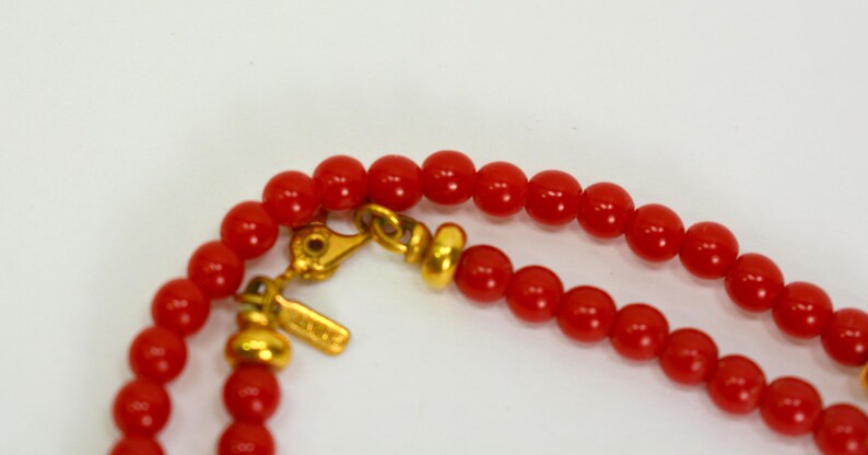 May include: A red beaded necklace with a gold clasp and a gold bead. The necklace is made of small, round beads.