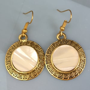Peut inclure: Boucles d'oreilles dorées avec une incrustation de nacre blanche et un motif de clé grecque.