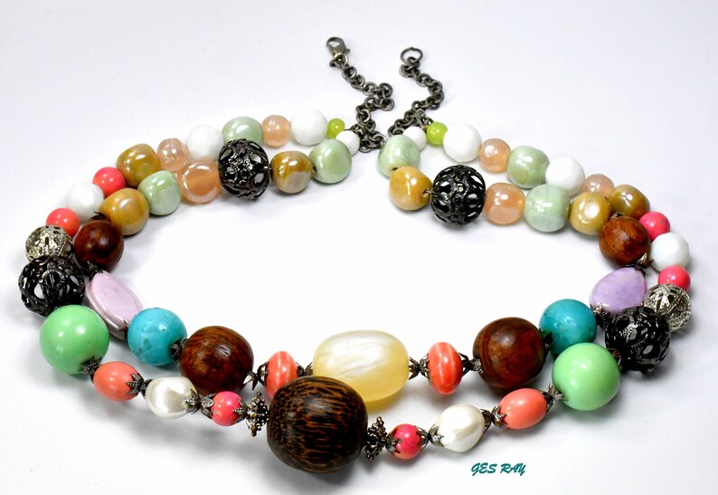 May include: A multi-strand necklace with a variety of colorful beads, including turquoise, pink, green, brown, and white. The necklace features metal accents and a large wooden bead.