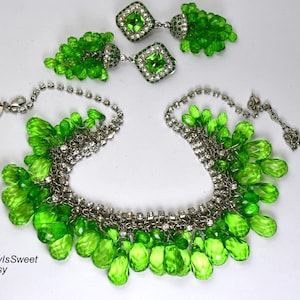 Puede incluir: Un deslumbrante conjunto de joyas con un collar y pendientes a juego. El conjunto presenta cuentas de vidrio verde brillante facetadas y metal plateado brillante. Los pendientes tienen piedras centrales verdes cuadradas. Un accesorio de moda llamativo.